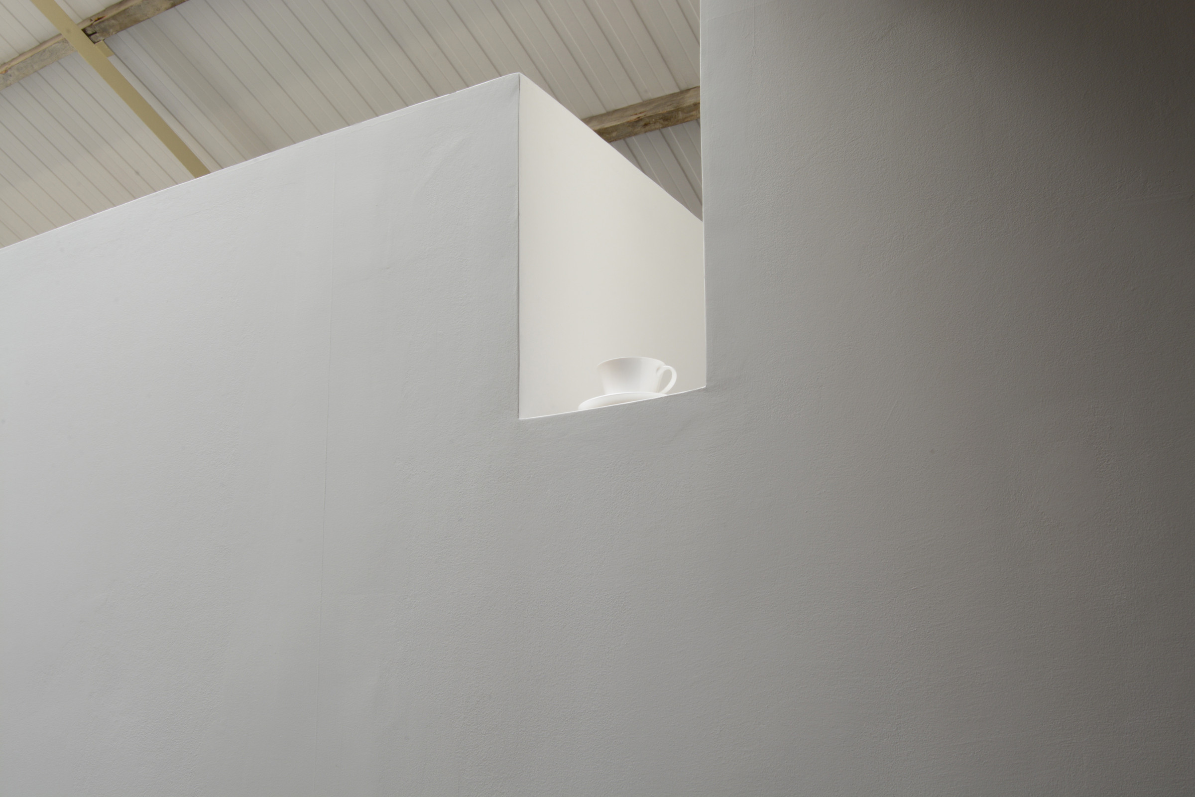 A white porcelain cup and saucer set high into a recess in a gallery wall